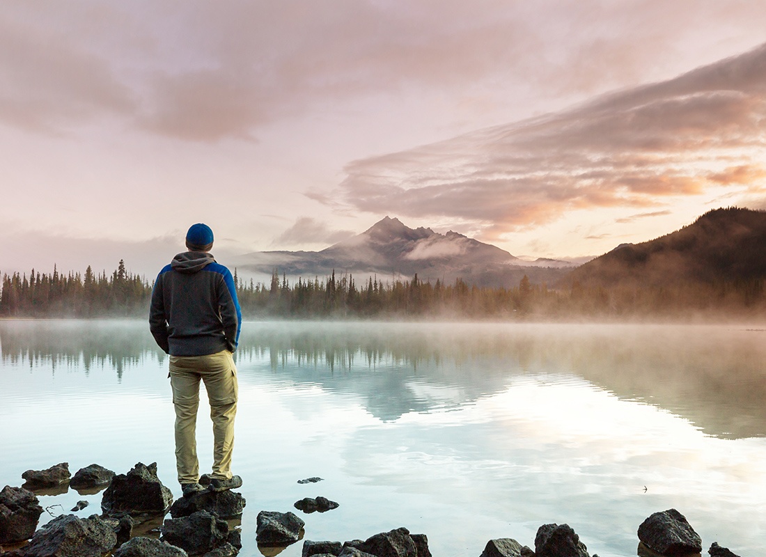 Insurance Solutions - Man Stands at the Edge of a Misty Lake With Mountains Behind it